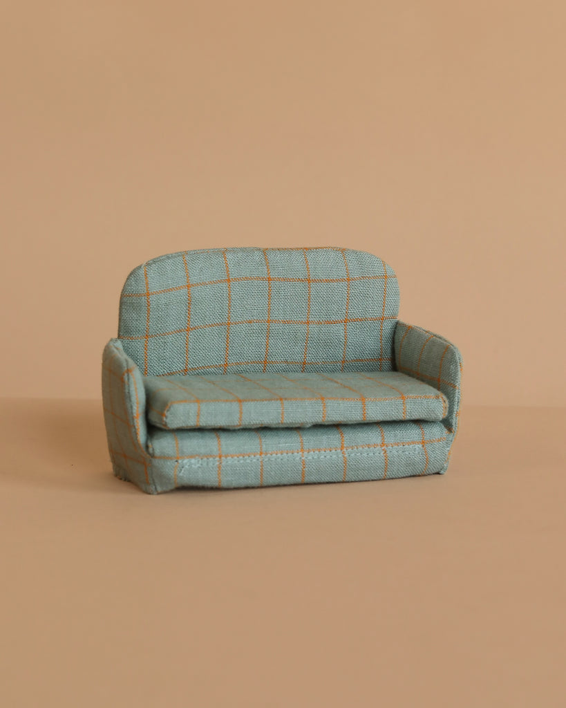 The Maileg Fully Furnished SuitCasa features a small, light blue sofa with yellow checks and rounded arms, set against a beige background—perfect for a mouse house or pairing with Maileg kitchen accessories.