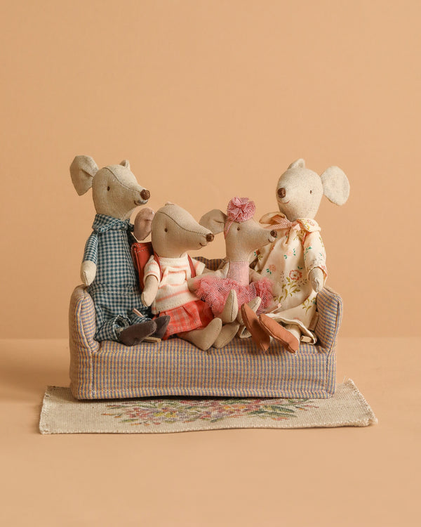The Maileg Family Set features four mice in colorful outfits sitting on a mouse couch, arranged on a patterned flower rug against a plain beige backdrop.