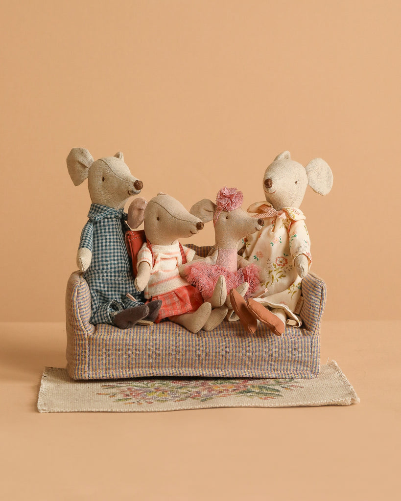 The Maileg Family Set features four mice in colorful outfits sitting on a mouse couch, arranged on a patterned flower rug against a plain beige backdrop.