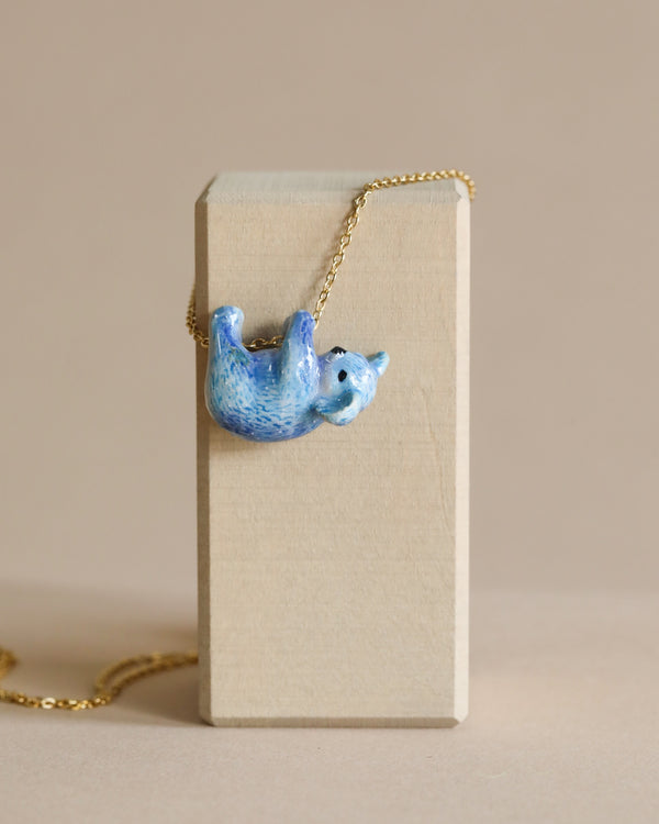 The Galaxy Bear Koala Necklace hangs on a 24k gold plated steel chain, draped over a tall rectangular cardboard box on a beige background.