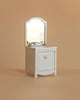 The Maileg Bathroom Set is a miniature white sink dresser with a mirrored back, gold faucets, and a single cabinet door—ideal as Maileg mouse furniture—shown against a beige background.
