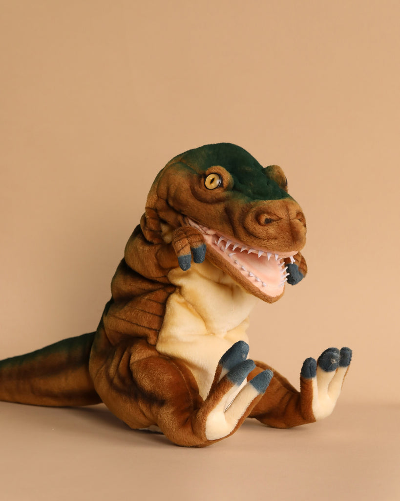 A T-Rex Dinosaur Puppet, featuring realistic details and a unique personality, is showcased against a light brown background. This hand-sewn plush toy displays a wide open mouth with visible white teeth and striking blue-tipped claws on its small arms and feet, highlighted by its brown and green hues.