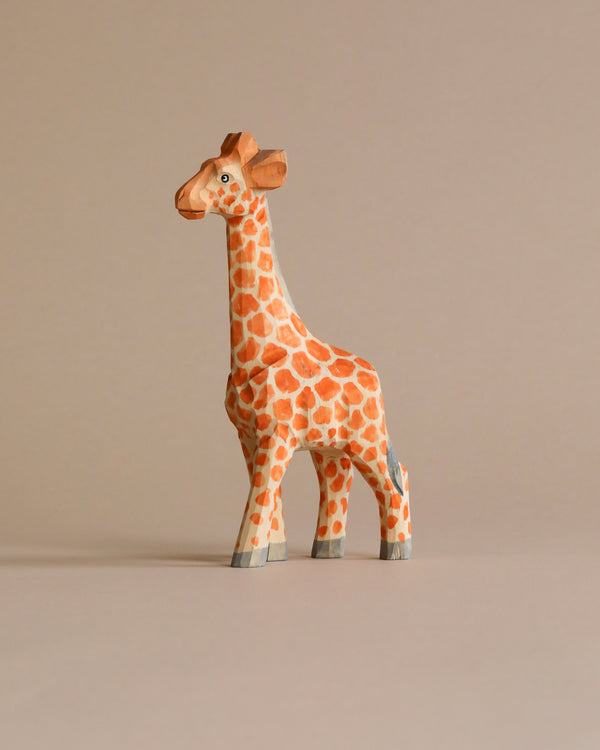 A colorful, Hand Carved Wooden Giraffe figurine with intricate patterns stands against a plain, light beige background.