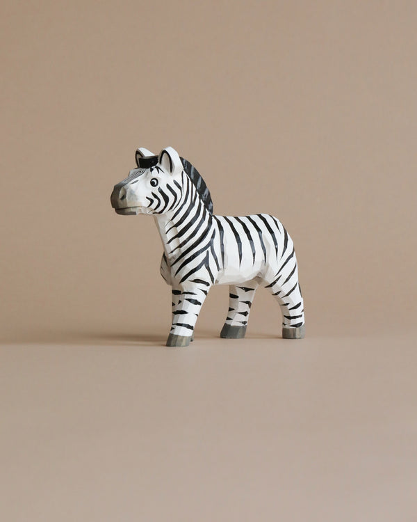 A Hand Carved Wooden Zebra toy with black and white stripes, standing upright on a plain beige background. This hand-carved animal toy features prominent stripes, ears, and a tail, depicted in a naturalistic
