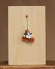 The Christian Ulbricht Ornament - Snowman on Sled features fine German craftsmanship, with a snowman in a hat and scarf on a sled, hanging from a red string against a wooden board on a simple background.