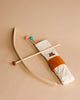 A traditional wooden Wooden Bow & Arrows Set with Goal with colorful fletching on a beige background. The FSC wood bow features a white and brown fabric grip.