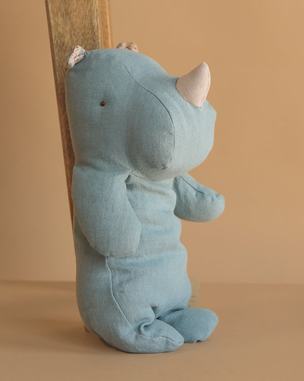 The Maileg Medium Rhino - Dusty Blue, featuring a soft white horn, sits upright against a wooden plank on a beige background, ready to join your collection of Safari friends.