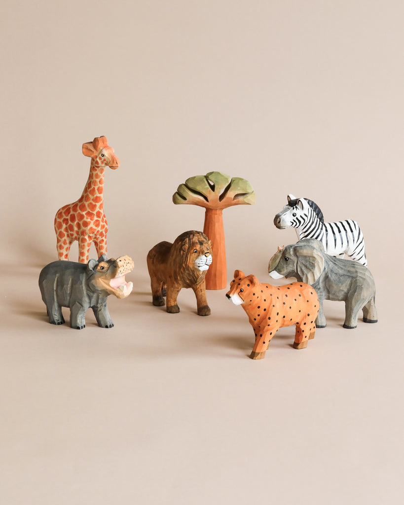 A collection of hand-carved wooden animal figurines, including a giraffe, Hand Carved Wooden Lion, elephant, zebra, cheetah, and a tree, arranged on a beige background.