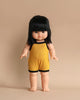 A Minikane Clothed Standing Doll (14.5") - Jade-Lou, with straight black hair and bangs, dressed in a yellow sleeveless romper with black trim, stands upright against a beige background. This anatomically correct doll has a neutral facial expression, is barefoot, and carries a gentle vanilla scent.