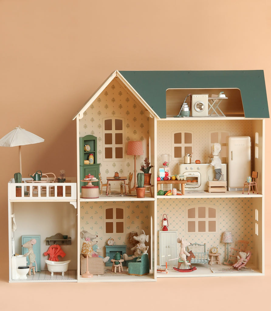 The Maileg Fully Furnished Dollhouse Set + Surprise Gift features five decorated rooms, a balcony, adorable furniture, and animal figurines—including a miniature bathroom—set against a peach background.