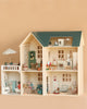 The Maileg Fully Furnished Dollhouse Set + Surprise Gift features multiple rooms, charming dollhouse furniture, small animal figurines, a miniature bathroom, and a rooftop patio with umbrella—all set against a plain beige background.