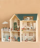 The Maileg Fully Furnished Dollhouse Set + Surprise Gift features multiple rooms, charming dollhouse furniture, small animal figurines, a miniature bathroom, and a rooftop patio with umbrella—all set against a plain beige background.