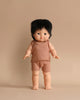 A Minikane Clothed Standing Doll (14.5") - Jude-Léo with straight dark hair and bangs stands against a beige background. The doll, featuring an anatomically correct design, is wearing a matching ribbed sleeveless top and shorts in a light brown color. Its arms and legs are slightly outstretched, exuding charm.