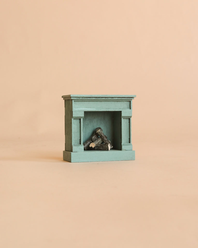 A Maileg Fireplace, Mouse—a small teal vintage fireplace featuring miniature logs inside—is displayed against a plain beige background.