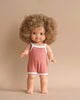 A Minikane Clothed Standing Doll (14.5") - Lise-Anaïs stands barefoot against a beige background, exuding a natural vanilla scent. It is wearing a pink sleeveless romper with white trim. The doll has a neutral expression and extends its arms slightly forward.