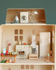 Create playful scenes with the Maileg Fully Furnished Dollhouse Set + Surprise Gift, featuring a toy chef, vintage stove, fridge, kitchen furniture, upstairs laundry area, and a peek at the miniature bathroom for added fun.