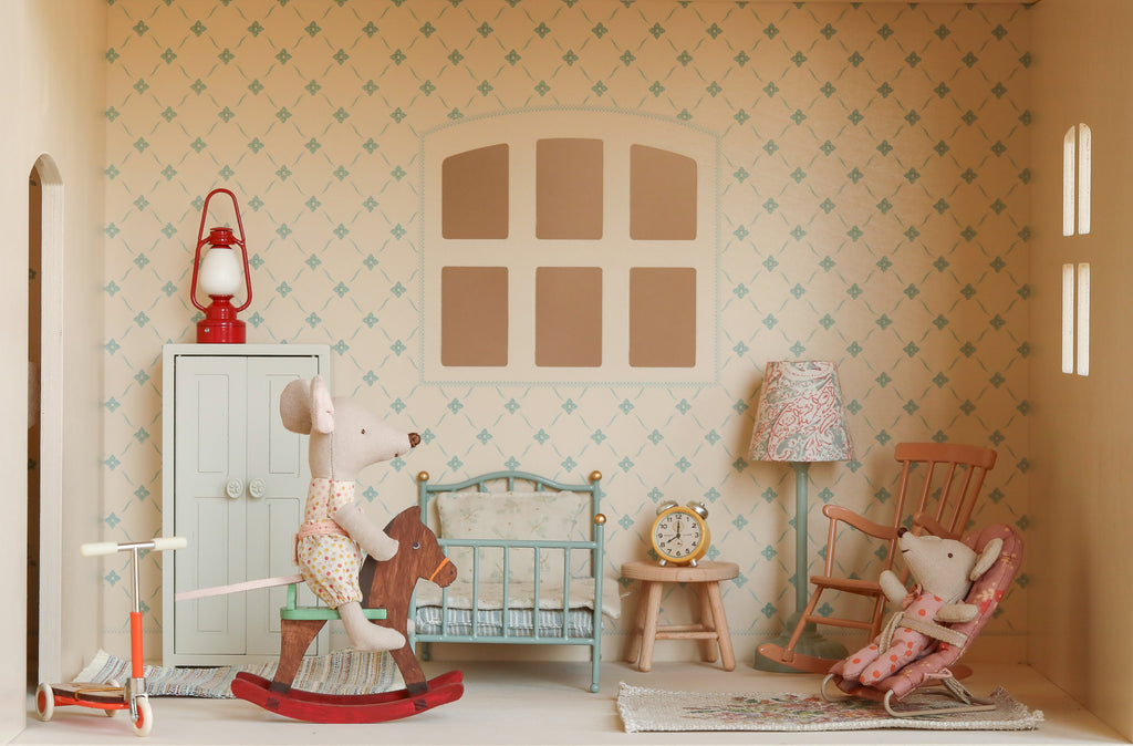 The Maileg Fully Furnished Dollhouse Set + Surprise Gift includes two toy mice (one on a rocking horse, one on a rocking chair), plus bed, wardrobe, scooter, red lantern, lamp, clock, and a four-pane window with patterned wallpaper.