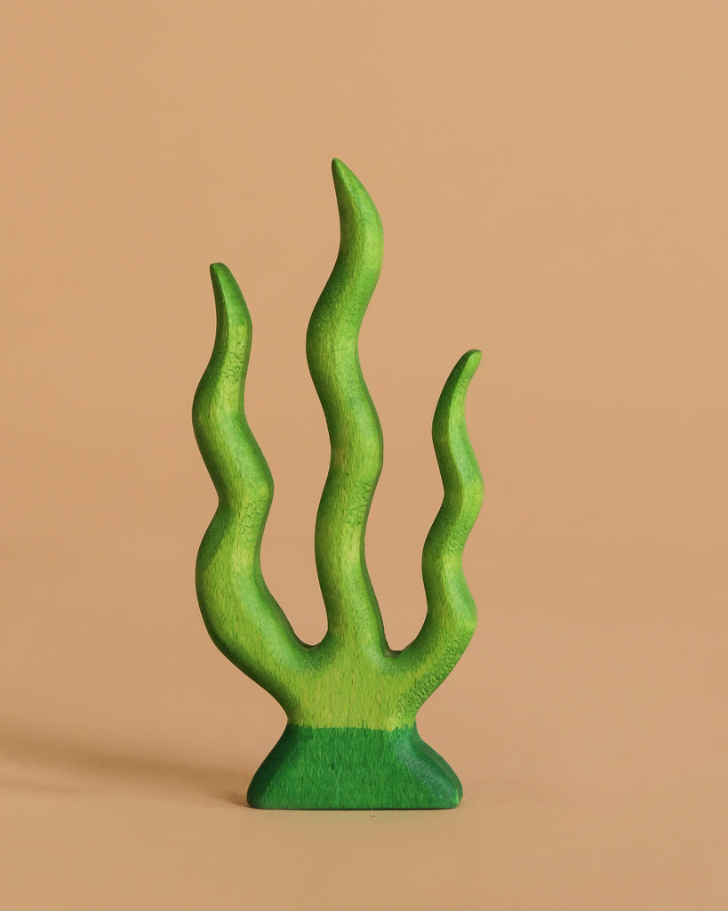 The Handmade Holzwald Underwater World Set features a small green wooden toy with four wavy branches, resembling seaweed, standing upright against a plain beige background.