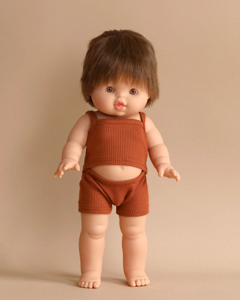 The Minikane Standing Doll (14") - Julian With Clothing, featuring short brown hair, is barefoot and dressed in a sleeveless brown top with matching shorts, posed against a beige background.