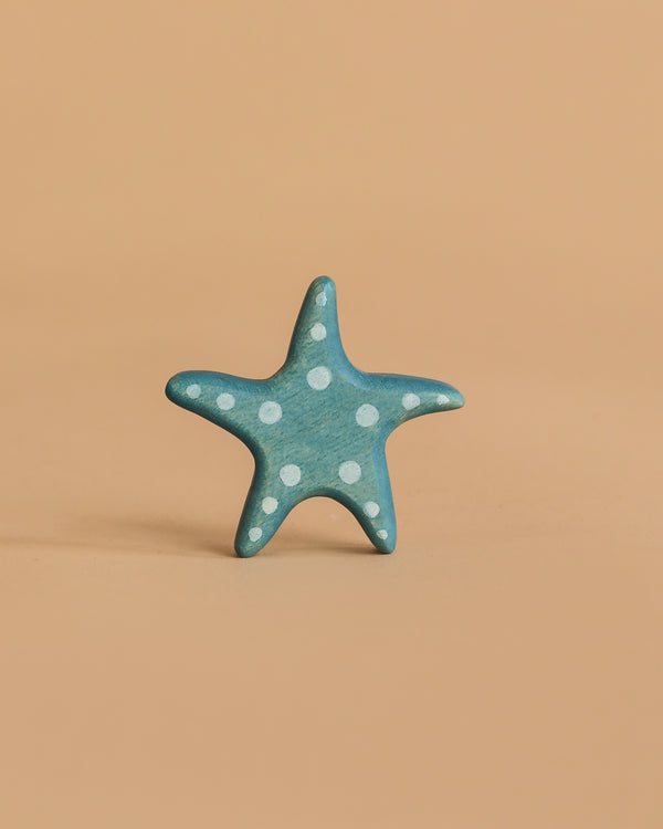 The Handmade Holzwald Starfish is a small blue wooden toy with white polka dots, shaped like a starfish and posed upright on a light brown surface—an ideal pick for anyone seeking sustainable toys.