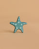 A small blue starfish with white polka dots from the Handmade Holzwald Ocean Animals Set sits upright on a plain light brown background.