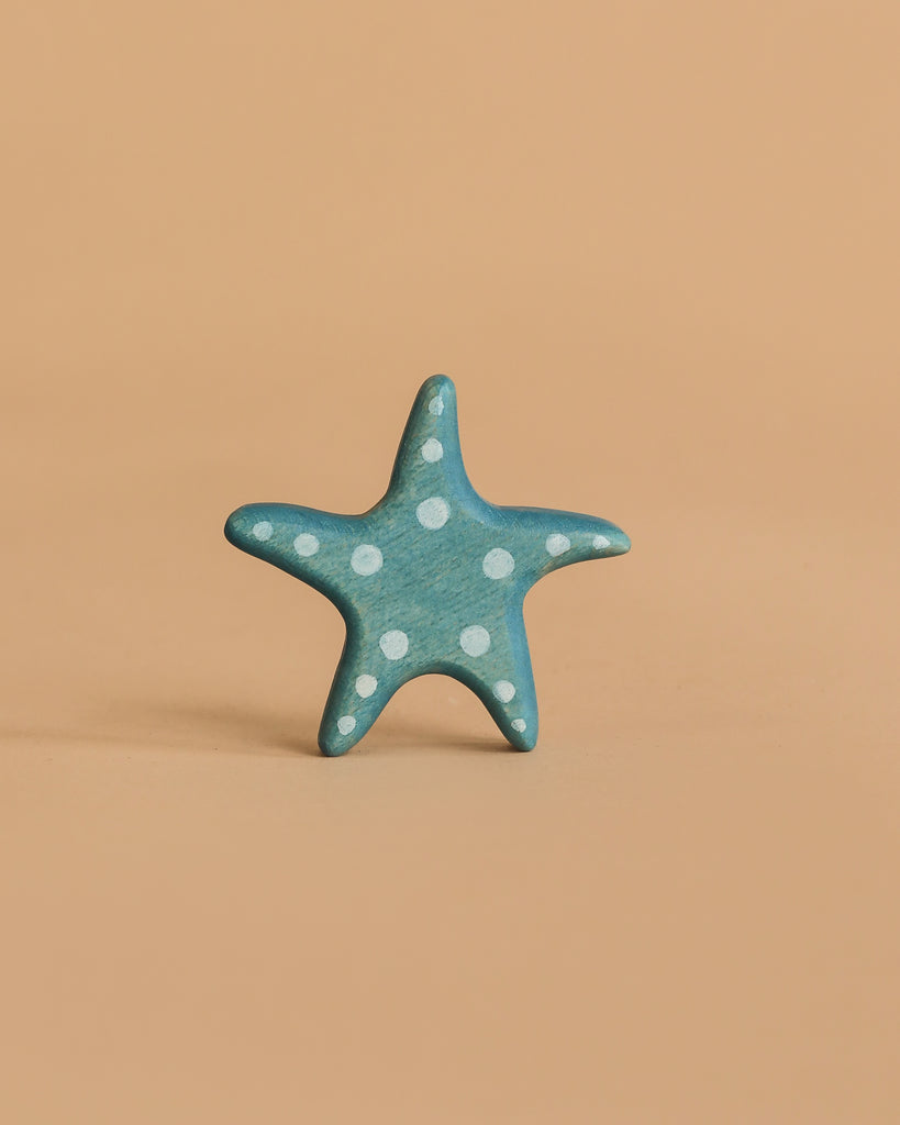 A small blue starfish with white polka dots from the Handmade Holzwald Ocean Animals Set sits upright on a plain light brown background.