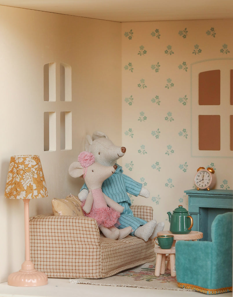 Two plush toy mice in knitted outfits sit on a checkered couch inside the Maileg Fully Furnished Dollhouse Set + Surprise Gift, surrounded by cozy furniture, a tea set, and florally wallpapered pastel living room accessories.