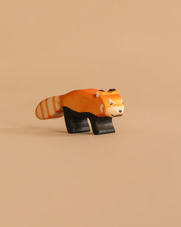 The Handmade Holzwald Red Panda is a handcrafted wooden figure featuring an orange and white striped tail, black legs, and a smiling face, displayed against a plain beige background.