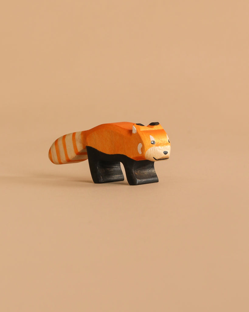 The Handmade Holzwald Red Panda is a handcrafted wooden figure featuring an orange and white striped tail, black legs, and a smiling face, displayed against a plain beige background.