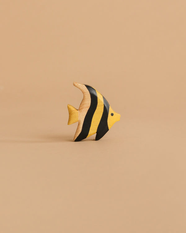 The Handmade Holzwald Moorish Idol Fish is a small, hand-painted wooden toy with yellow and black stripes, displayed on a beige surface—an enchanting piece for any collection of educational wooden toys.