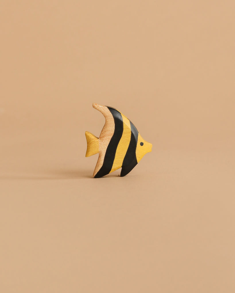 The Handmade Holzwald Moorish Idol Fish is a small, hand-painted wooden toy with yellow and black stripes, displayed on a beige surface—an enchanting piece for any collection of educational wooden toys.