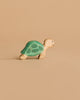 A small Handmade Holzwald Ocean Animals Set turtle toy, featuring a green shell and beige body, is displayed against a plain light brown background.
