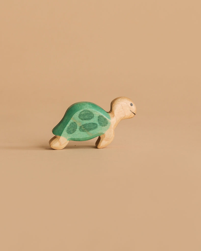 A small Handmade Holzwald Ocean Animals Set turtle toy, featuring a green shell and beige body, is displayed against a plain light brown background.