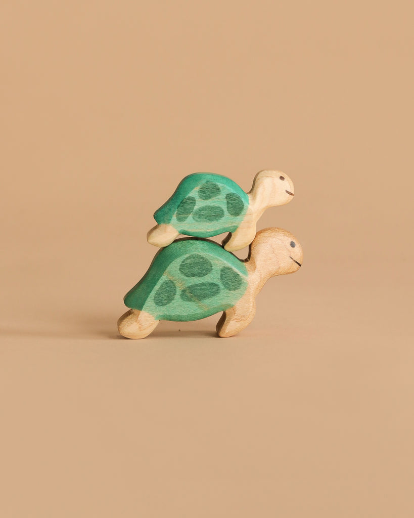 Two Handmade Holzwald Sea Turtle wooden toys, in green and beige, are stacked together against a plain beige background—ideal for creative underwater play setups.