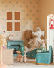 The Maileg Fully Furnished Dollhouse Set + Surprise Gift includes two fabric mice on blue chairs, a green fireplace, a clock, tea set, floral wallpaper, furniture, lamps, and charming decorations for a cozy living room.