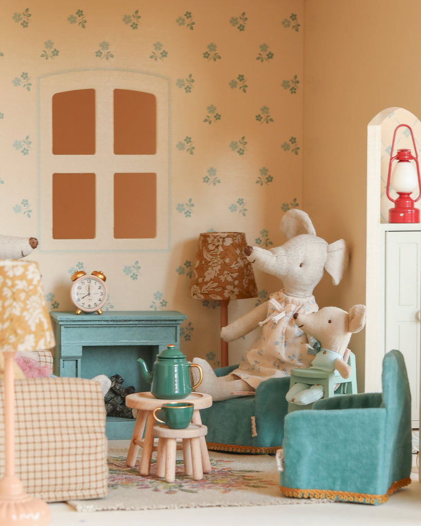 The Maileg Fully Furnished Dollhouse Set + Surprise Gift includes two fabric mice on blue chairs, a green fireplace, a clock, tea set, floral wallpaper, furniture, lamps, and charming decorations for a cozy living room.