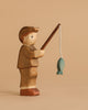 The Handmade Holzwald Fisherman is a nature-inspired wooden toy figure holding a fishing rod with a blue fish, set against a plain beige background. Ideal for those who appreciate handcrafted toys.