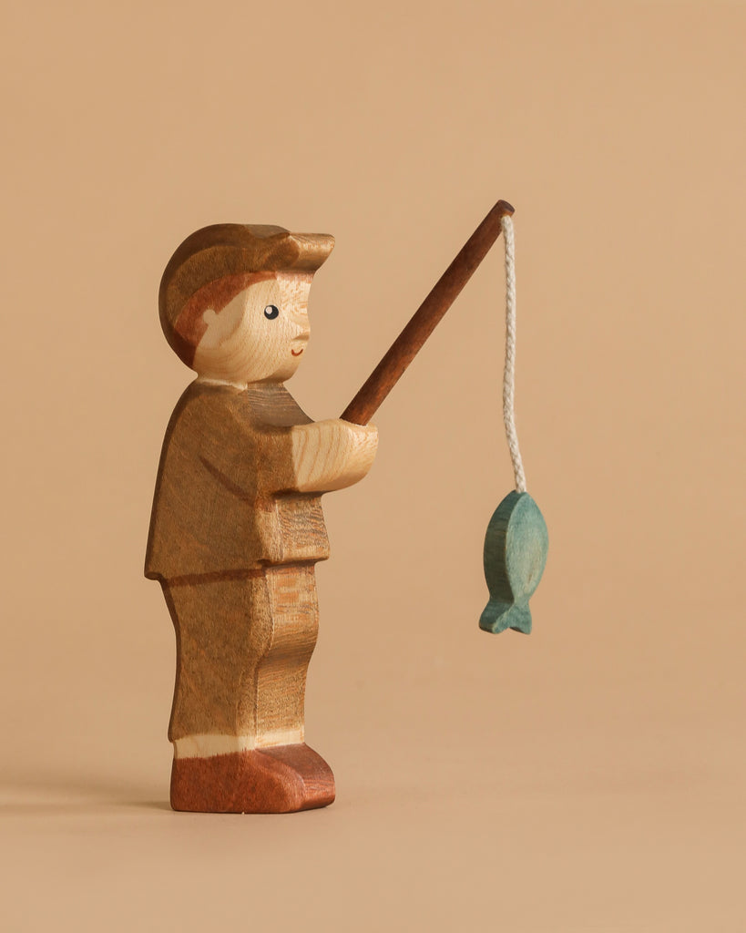 The Handmade Holzwald Fisherman is a nature-inspired wooden toy figure holding a fishing rod with a blue fish, set against a plain beige background. Ideal for those who appreciate handcrafted toys.