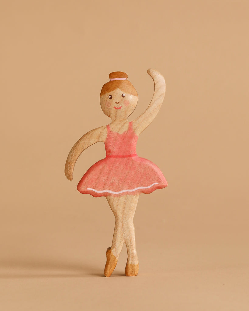 The Handmade Holzwald Ballerina, with a pink tutu and bun, stands en pointe against a plain beige background, smiling warmly—an ideal toy to spark imaginative play.