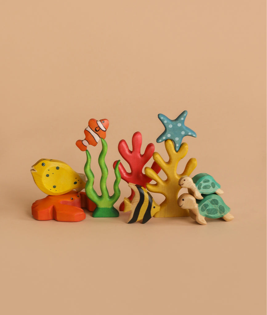 Handmade Holzwald Moorish Idol Fish with colorful wooden figures—clownfish, starfish, turtle, and green plants—are arranged on a light brown background to inspire ocean-themed play.