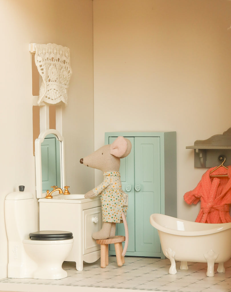 The Maileg Fully Furnished Dollhouse Set + Surprise Gift creates a cozy bathroom scene with a toy mouse in pajamas, dollhouse furniture like a toilet, bathtub, mint-green cabinet, tiled floor, mirror sink, and more charming mini details.