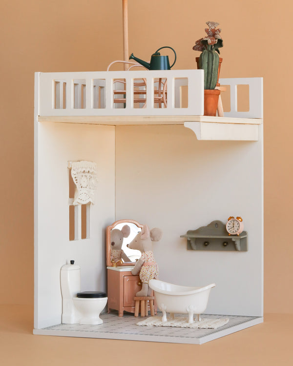 The Maileg Bonus Room Bathroom Set includes a mouse figurine, vanity, clawfoot tub, toilet, and crocheted wall hanging. Upstairs features House of Miniature accessories like a watering can and potted plant.