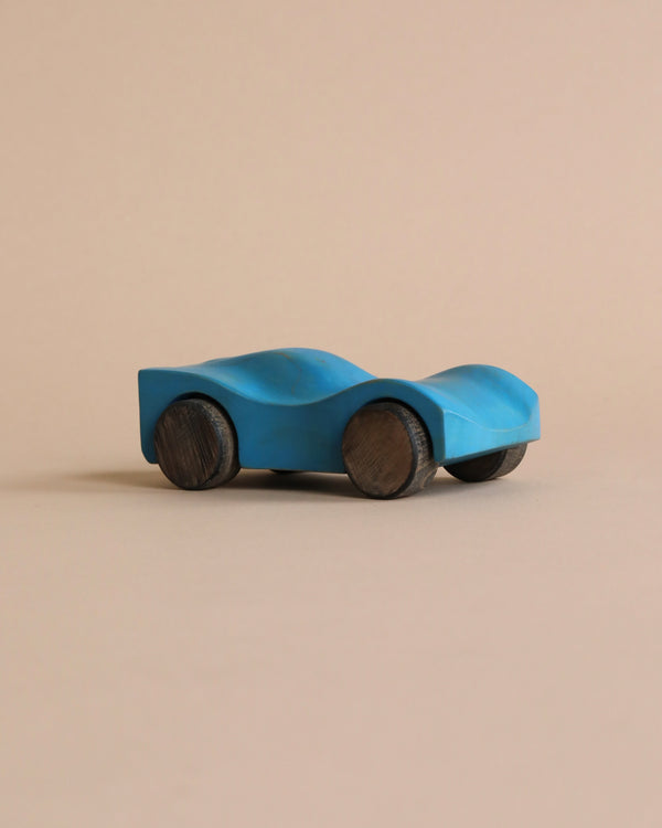 A Handmade Wooden Race Car - Blue crafted from Beech, featuring rounded wooden wheels, is displayed against a beige background. Coated in non-toxic paint, the car has a sleek, smooth design with no additional features or markings.