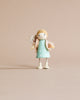 Mrs. Goodwood and her Baby, a small solid wood doll in a teal dress with polka dots and a beige scarf, holding a tiny white bear, stands against a plain light beige background.