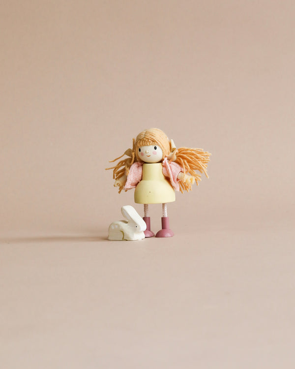 A small Amy and her Rabbit doll with blonde yarn hair, dressed in yellow and pink jersey fabrics, stands next to a tiny white rabbit figurine against a neutral background.