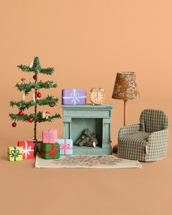 The Maileg Christmas Morning Living Room Set includes a fireplace, decorated Christmas tree, wrapped presents, floral lamp, dollhouse accessories, checkered armchair, and patterned rug arranged on a beige background.