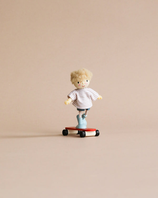 A small doll with blond hair and a striped shirt rides Edward and his Skateboard against a plain, light tan background.