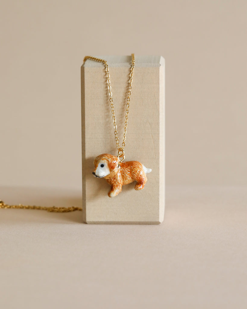 Golden Retriever Necklace with a pendant shaped like a golden retriever, hand painted, hangs from a beige display block against a neutral background.