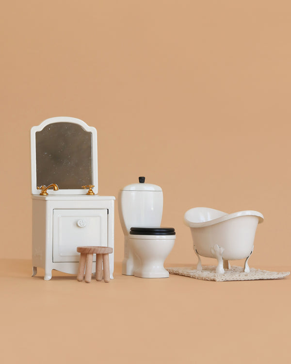 The Maileg Bathroom Set, shown on a beige background, includes a sink dresser, vanity with mirror and faucet, wooden stool, toilet, and clawfoot bathtub—ideal furniture for your Mouse Hole Farmhouse.