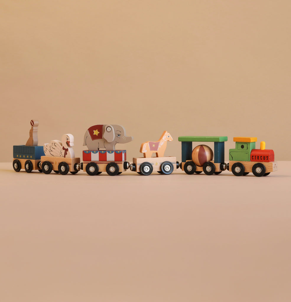 Konges Sloejd Wooden Animal Train featuring colorful beechwood cars carrying circus animals—a rabbit, lion, elephant, and giraffe—against a plain beige background. This charming magnetic train set is perfect for imaginative play.